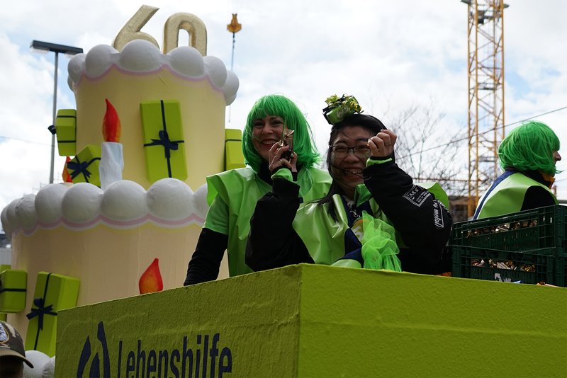 Grüner Karnevalswagen mit Riesentorte und drei Frauen mit grünen Perücken